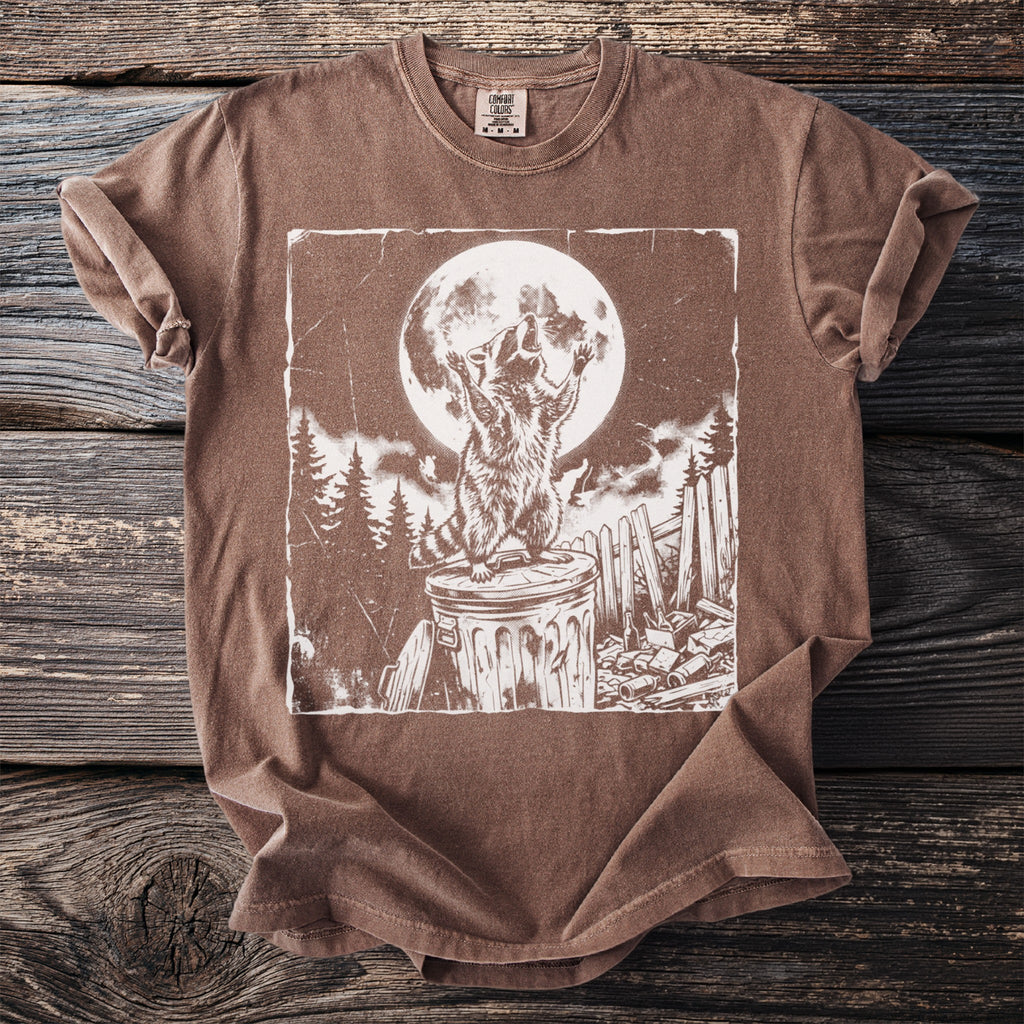Brown t-shirt with white graphic of raccoon on trash can under full moon.