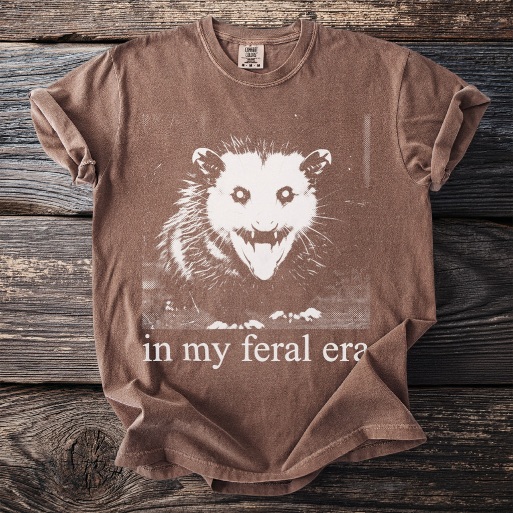 Brown t-shirt with white possum graphic and "in my feral era" text.