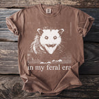Brown t-shirt with white possum graphic and "in my feral era" text.
