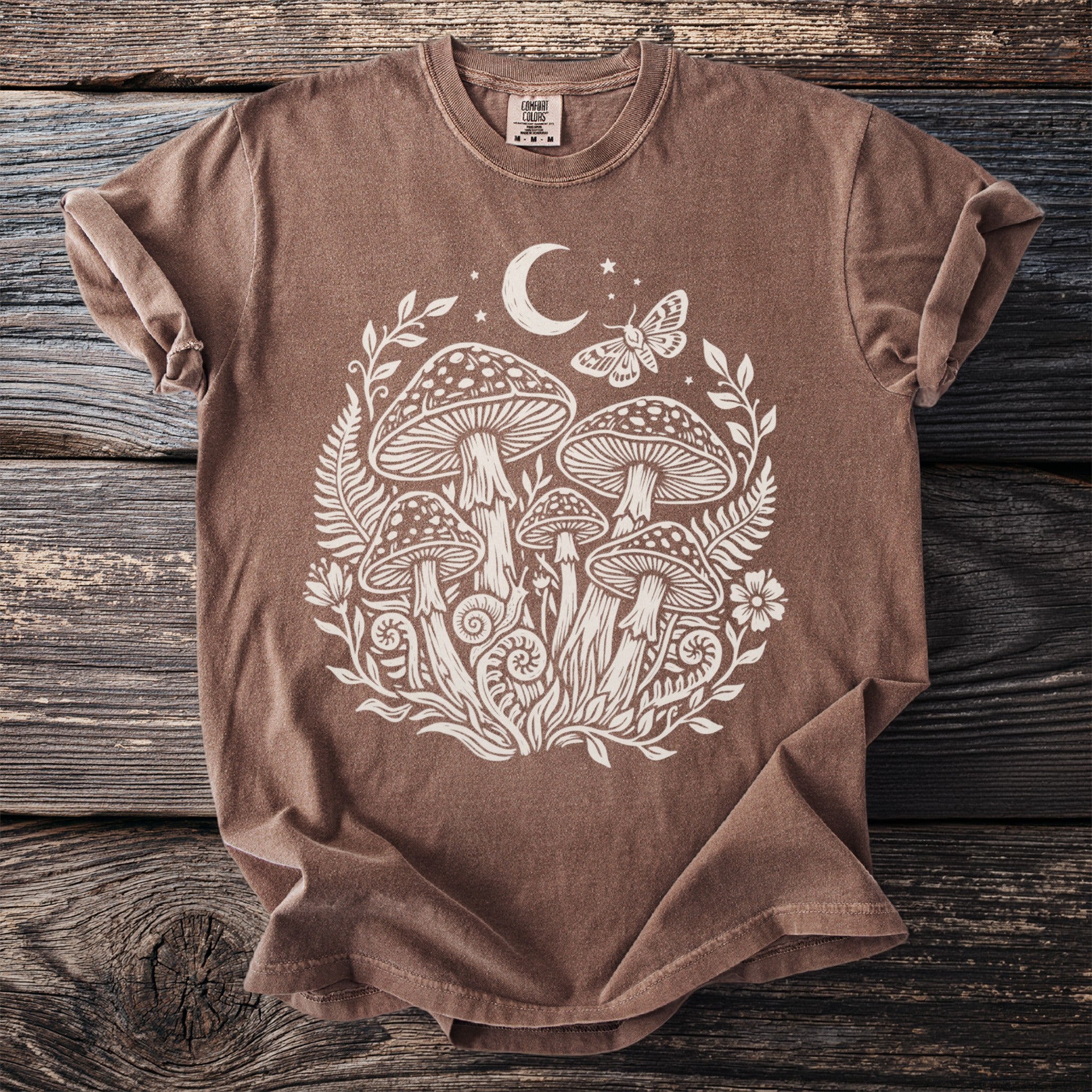 Brown t-shirt with white mushroom, moon, moth, and floral graphic.