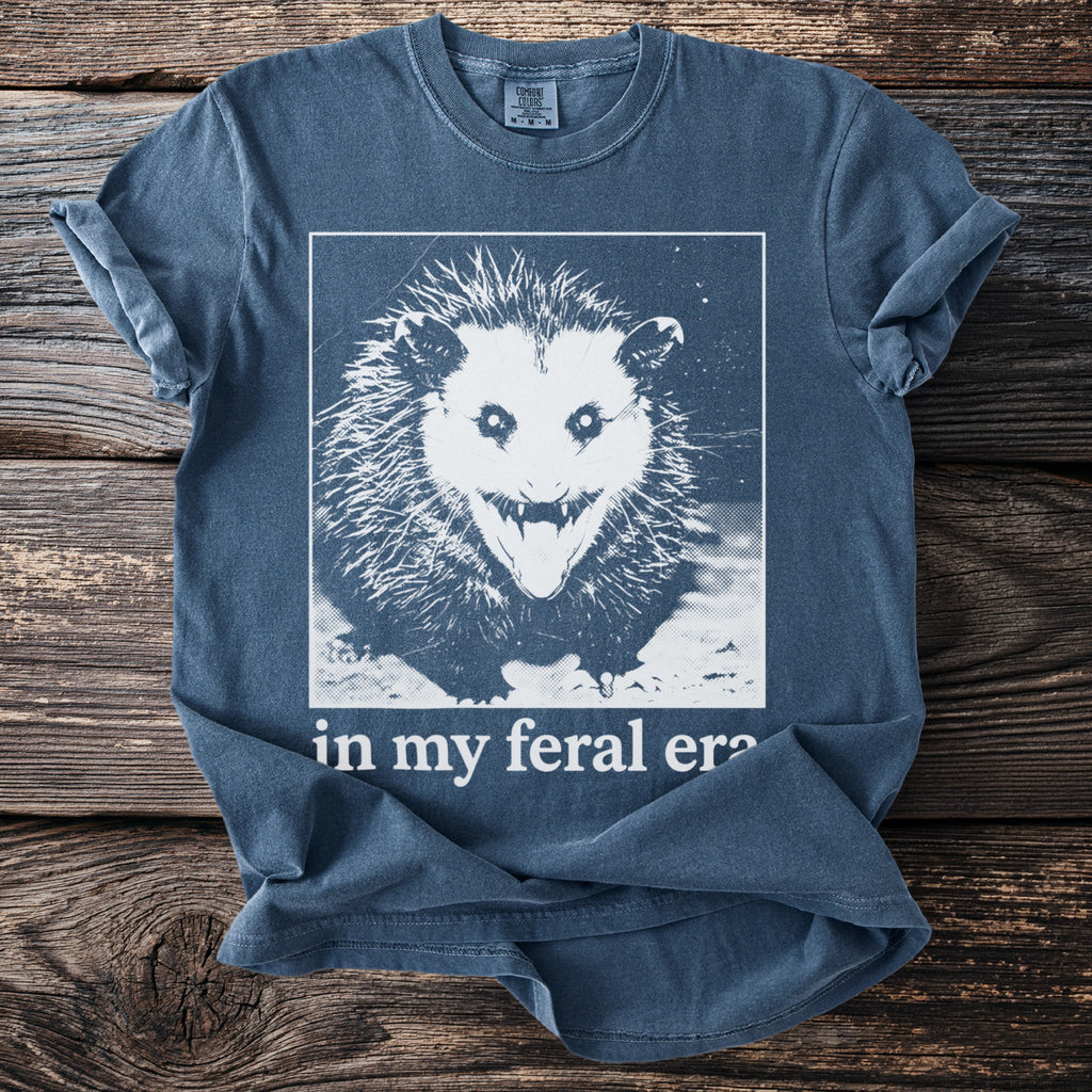Blue t-shirt with a white graphic of a screaming possum and text "in my feral era".