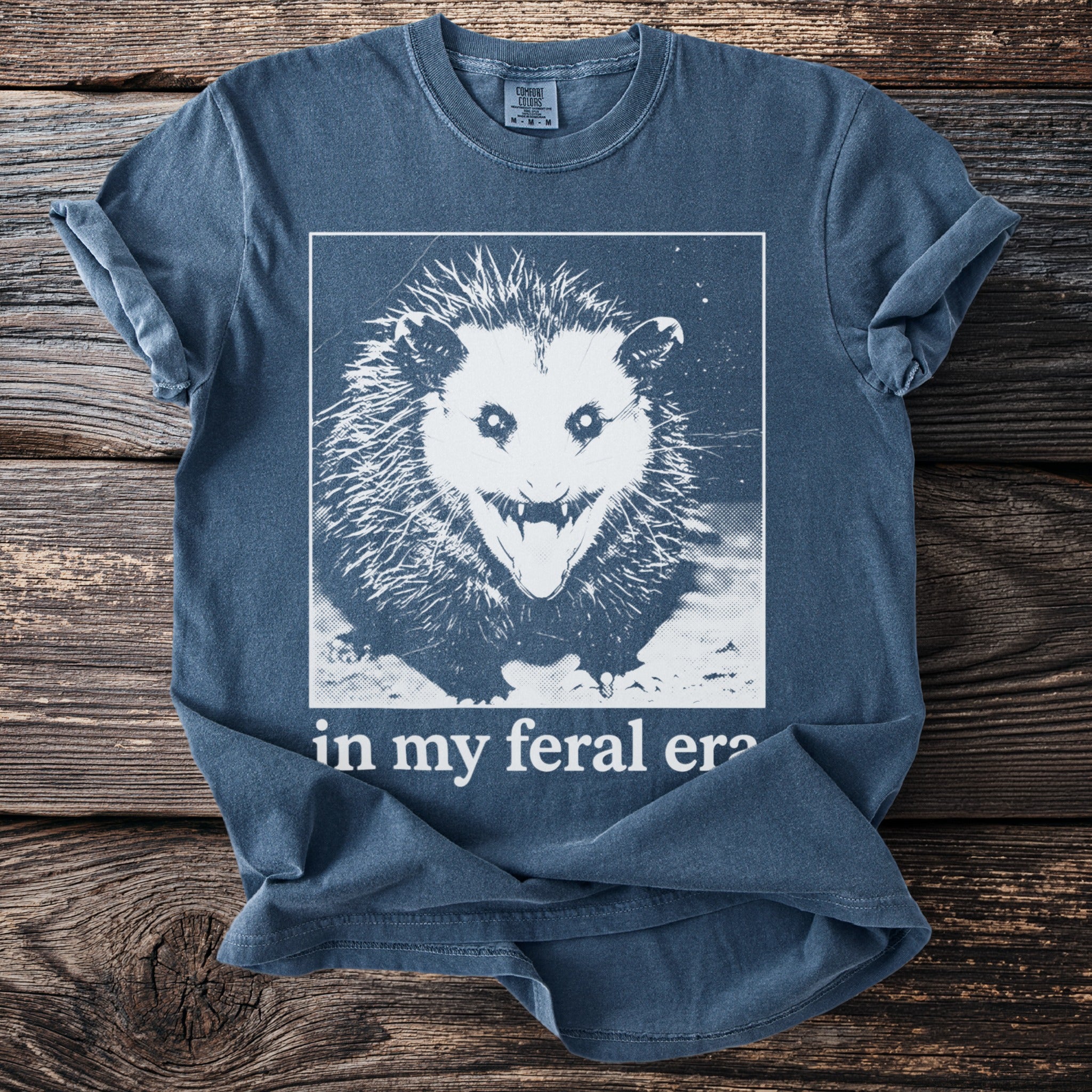 Blue t-shirt with a white graphic of a screaming possum and text "in my feral era".