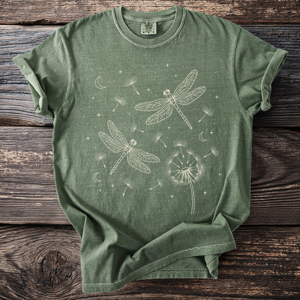 Green t-shirt with white graphic of dragonflies, dandelions, moons, and stars