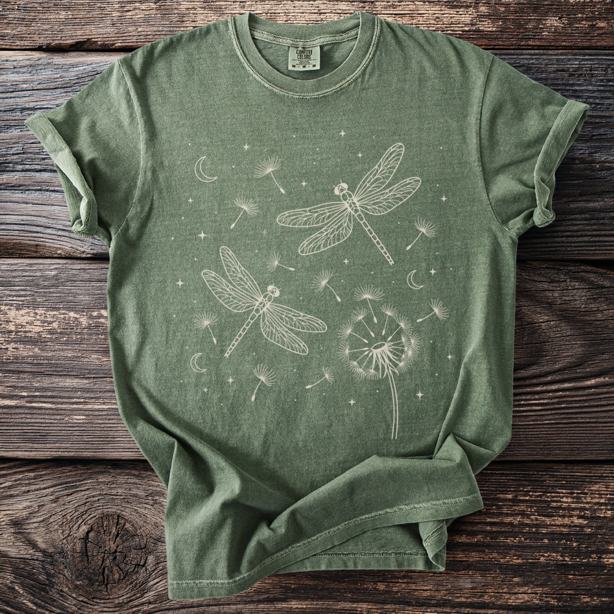 Green t-shirt with white graphic of dragonflies, dandelions, moons, and stars
