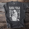 Baba Yaga illustration on a dark grey t-shirt with a wooden background.
