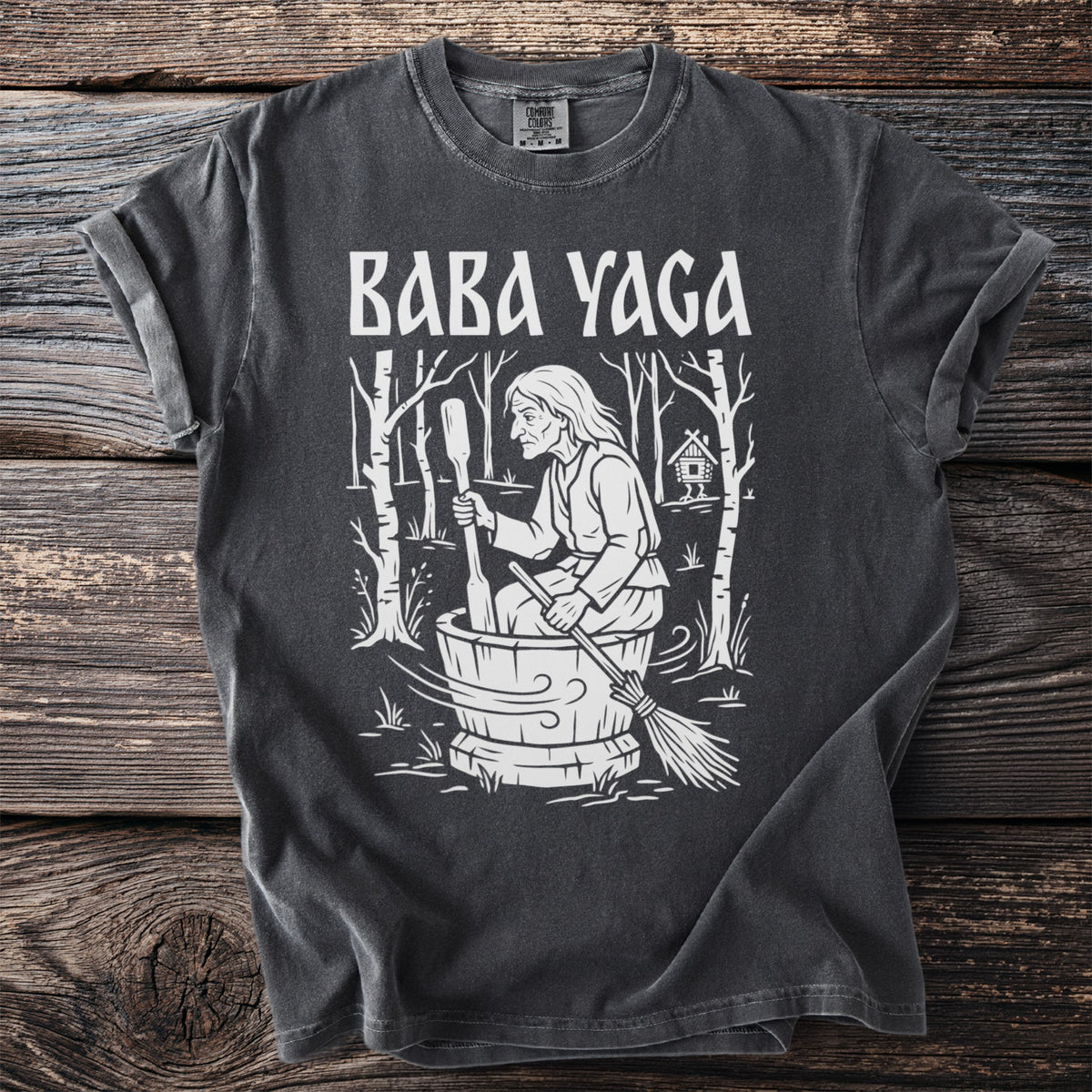 Baba Yaga illustration on a dark grey t-shirt with a wooden background.
