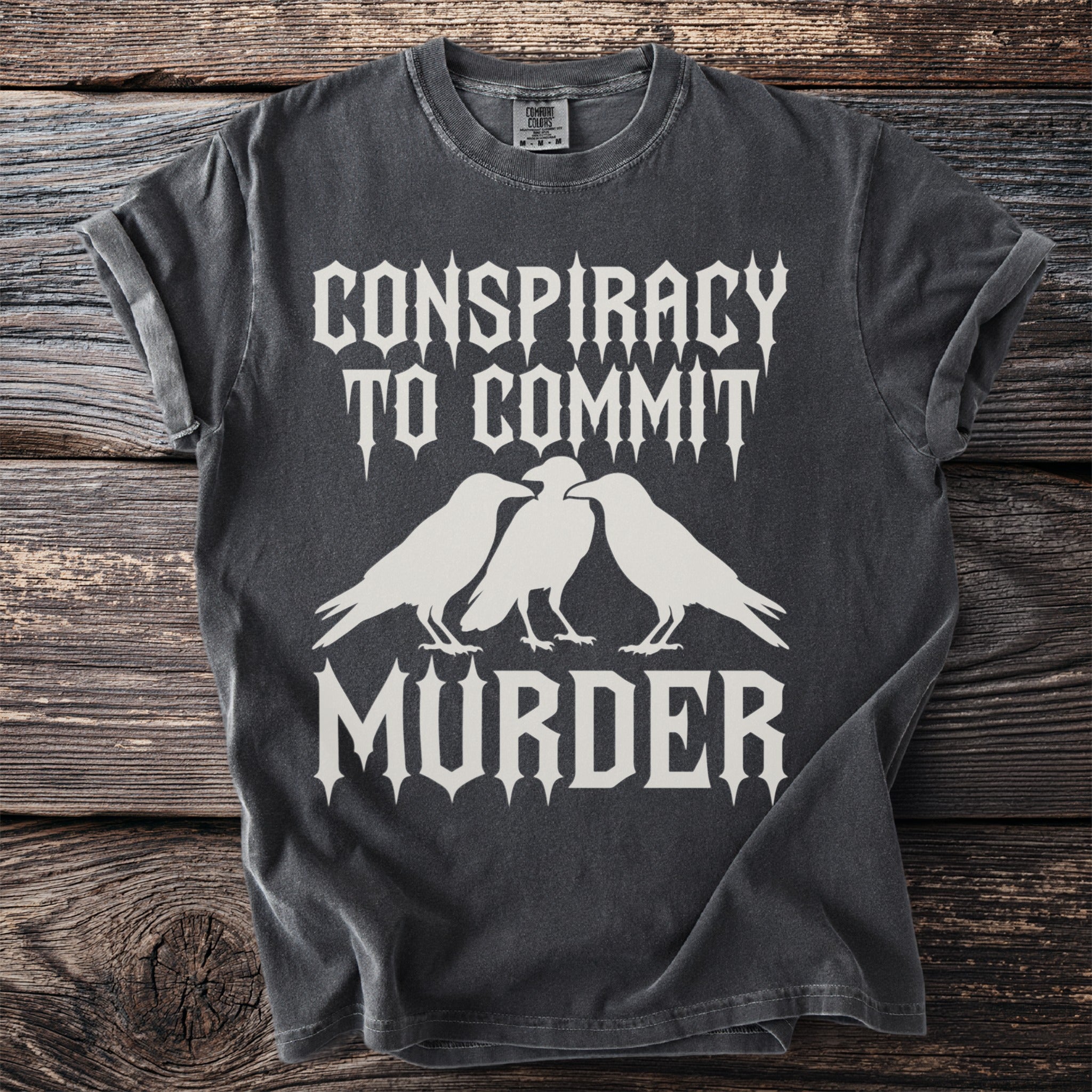 Dark gray t-shirt with white text "CONSPIRACY TO COMMIT MURDER" and three crows.