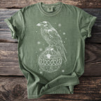 Raven perched on a decorative ornament with snowflakes on a green t-shirt.