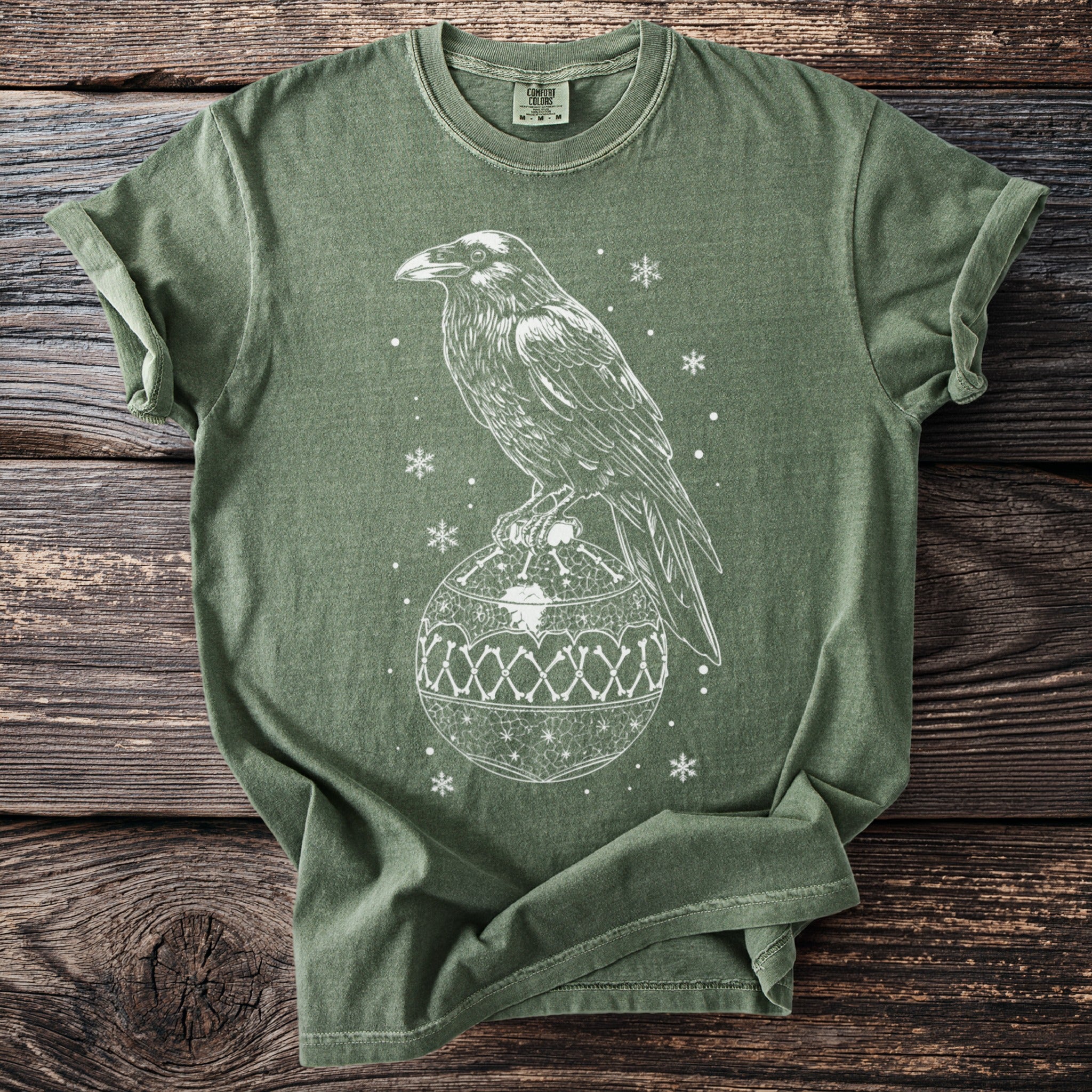 Raven perched on a decorative ornament with snowflakes on a green t-shirt.
