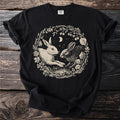 Black t-shirt featuring two rabbits in a circular floral and berry wreath with moon.