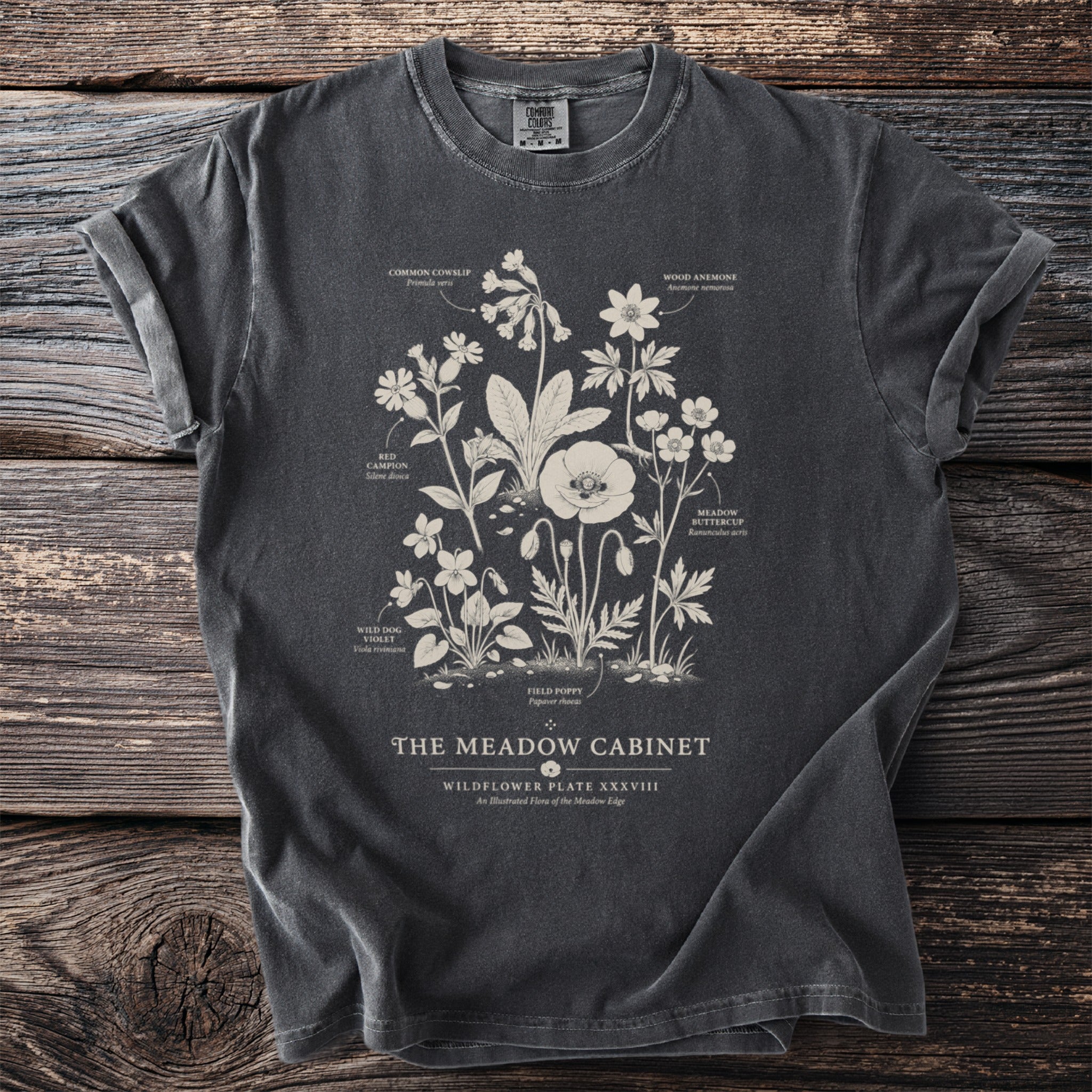 Dark t-shirt with wildflower illustration labeled "The Meadow Cabinet: Wildflower Plate XXXVIII".