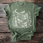 Green t-shirt with white graphic of stacked books, candle, key, moth, and moon.