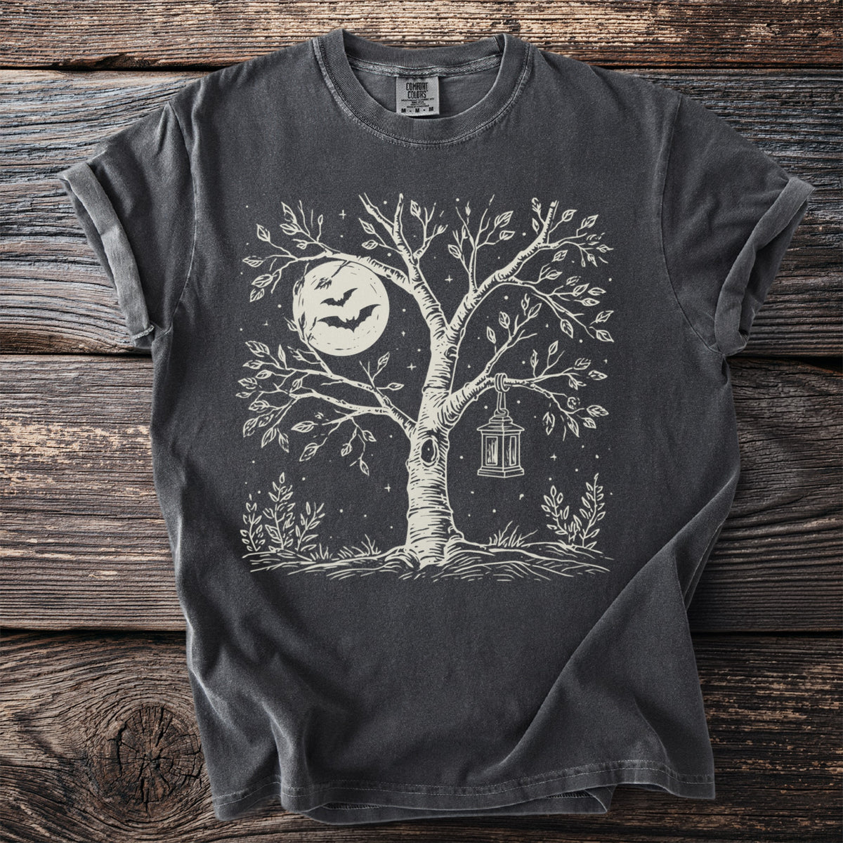 Dark t-shirt with a white linocut design of a tree, moon, bats, and lantern.
