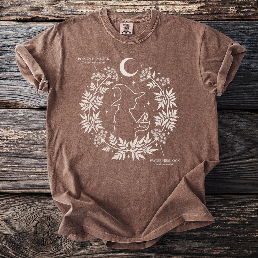 Brown t-shirt with white witch silhouette, moon, and botanical illustrations.