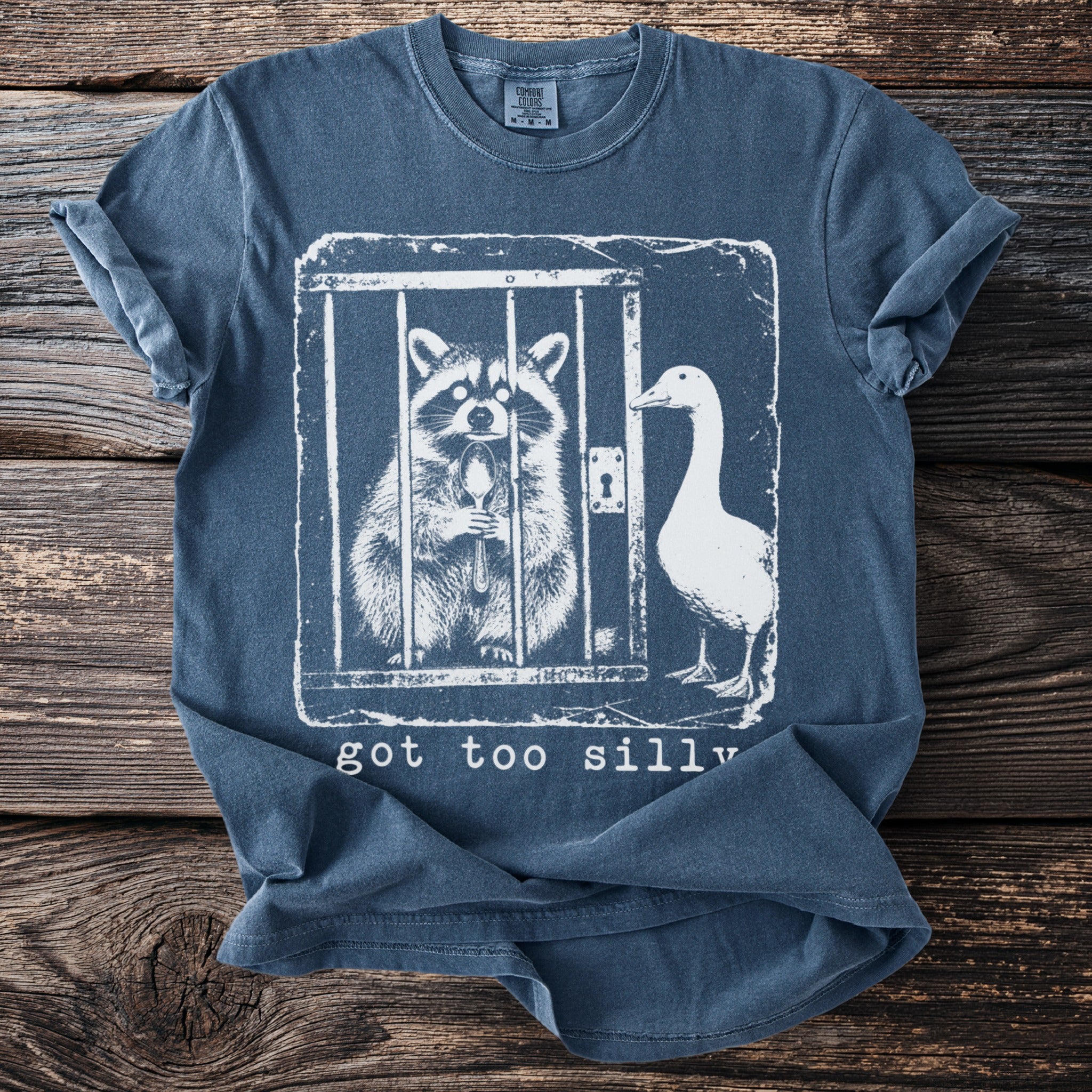 T-shirt graphic with raccoon inside cage holding spoon and duck outside, reads "got too silly".