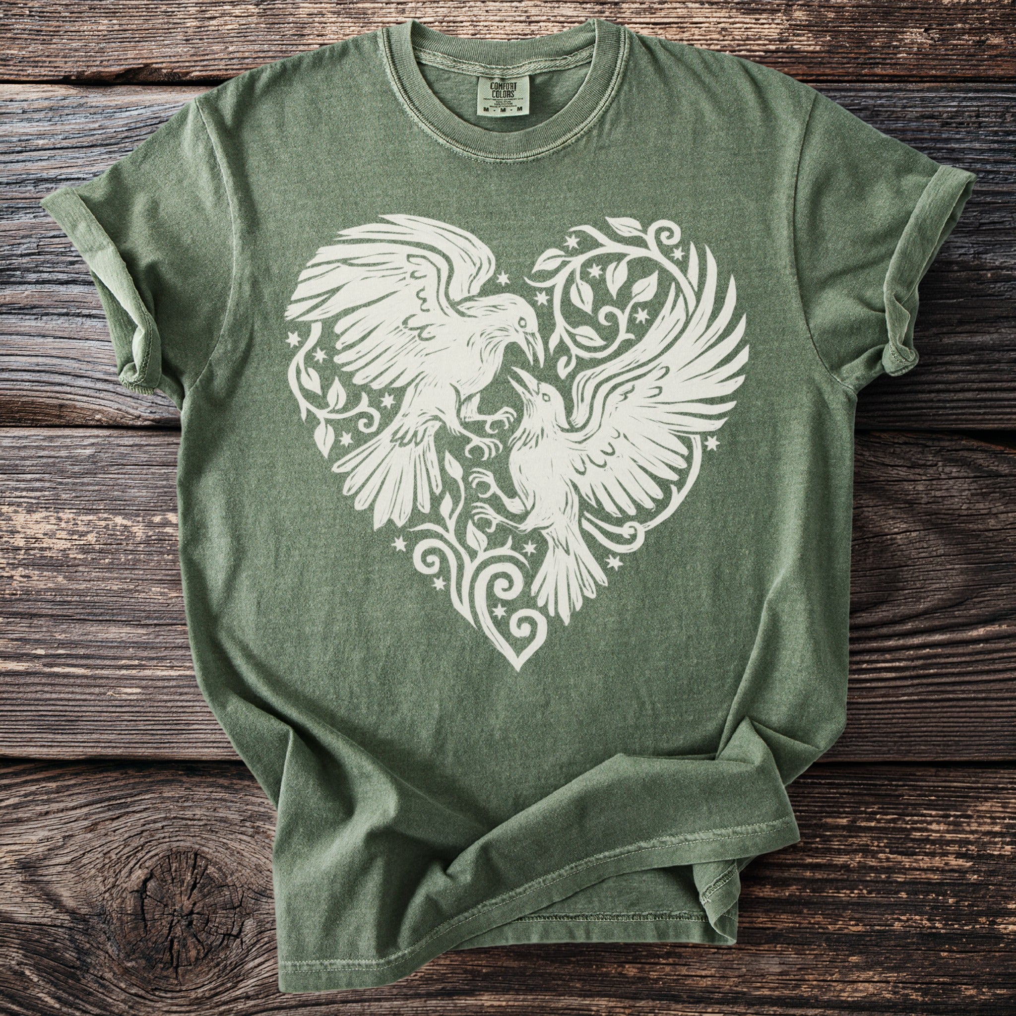 Olive green t-shirt with white linework design of two birds within a heart shape.