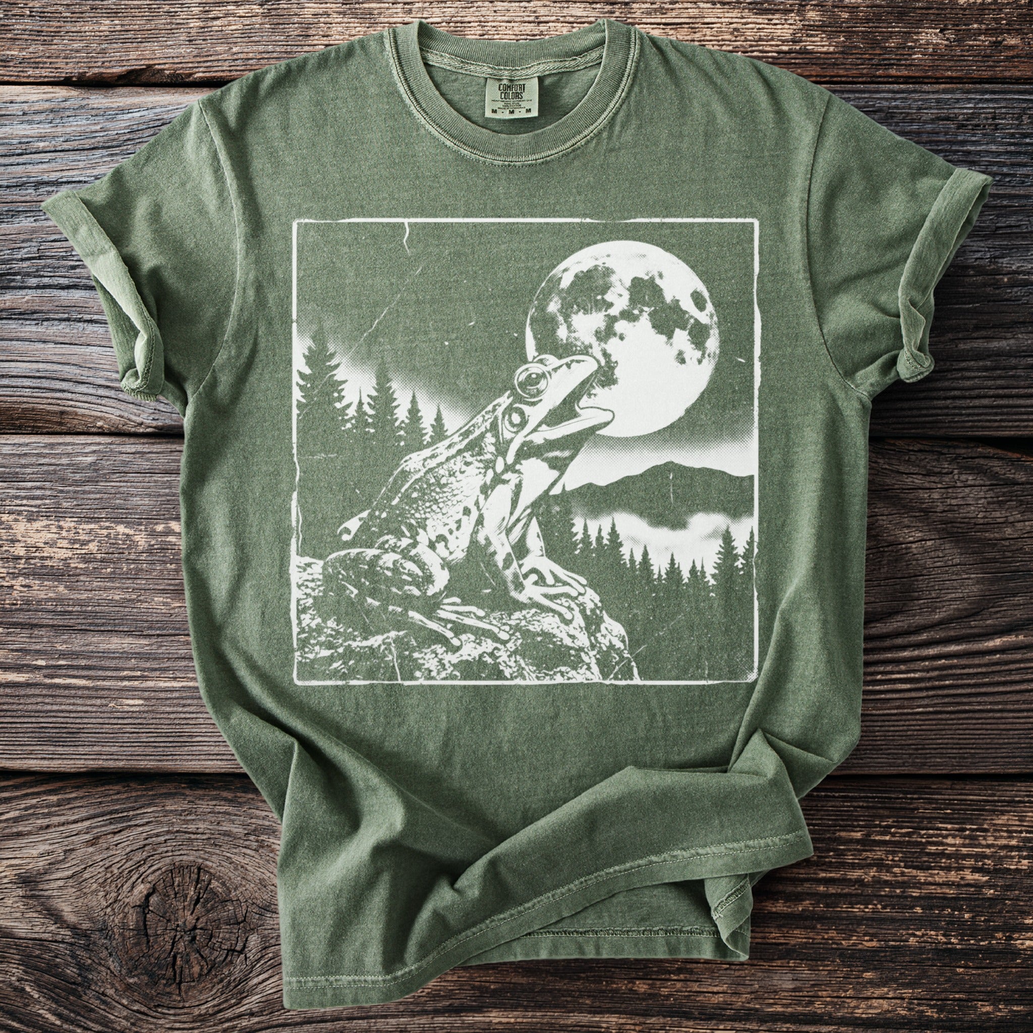 Green t-shirt with a white graphic of a frog on a rock under the moon.