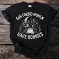 Black t-shirt with white graphic of three cats, a cauldron, and the text "GOD FORBID WOMEN HAVE HOBBIES".