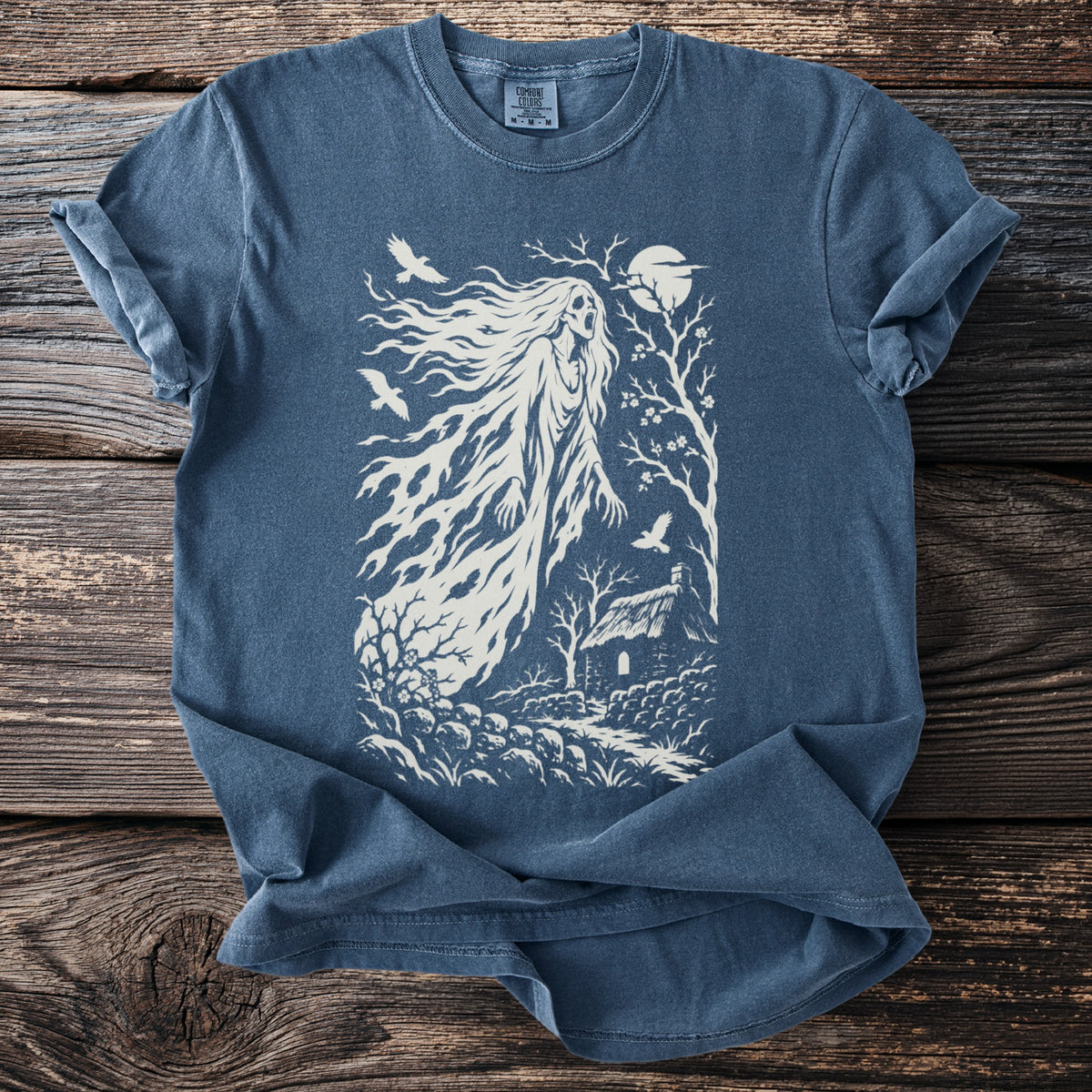 Blue t-shirt with white graphic of a ghost, cottage, birds, and moon.