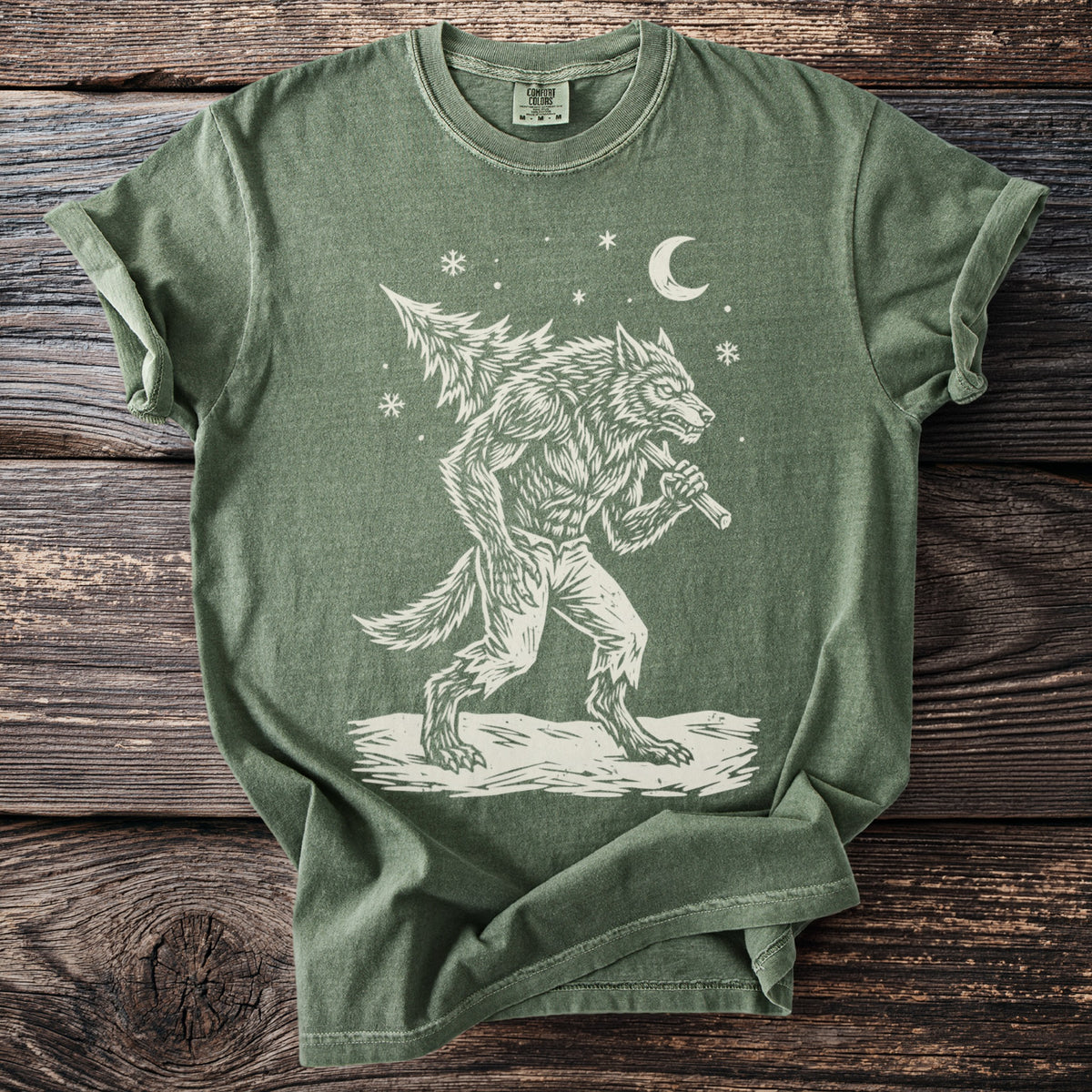 Moss green t-shirt with a cream folk-cut print: a snarling werewolf in torn trousers walks through the snow with a fir tree over his shoulder.