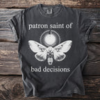 Dark t-shirt with a moth and lightbulb graphic, text reads "patron saint of bad decisions".