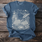 Blue t-shirt with white graphic of a cat, candle, open book, and mushrooms.