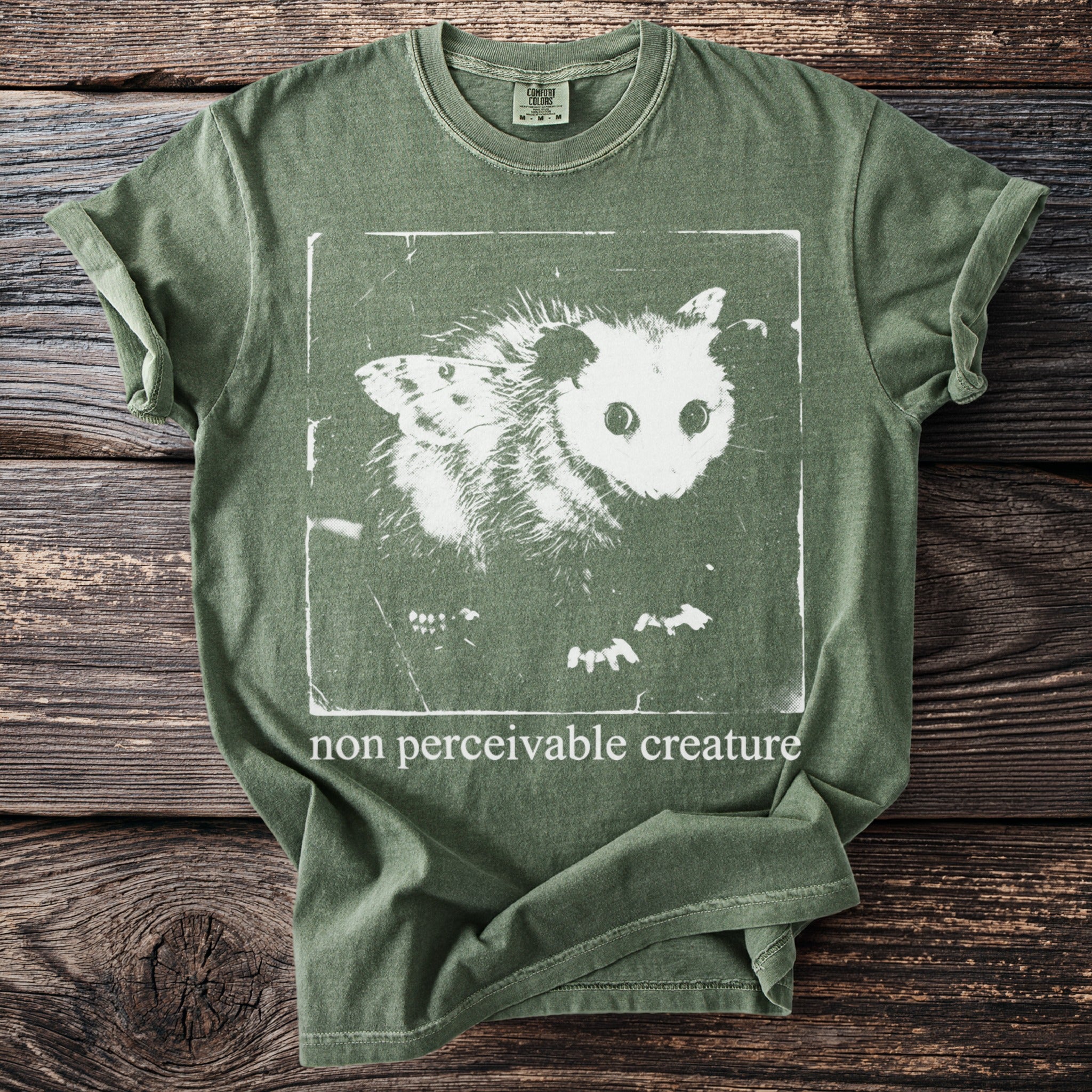 Green t-shirt with a white graphic of a possum with butterfly wings and the text "non perceivable creature."