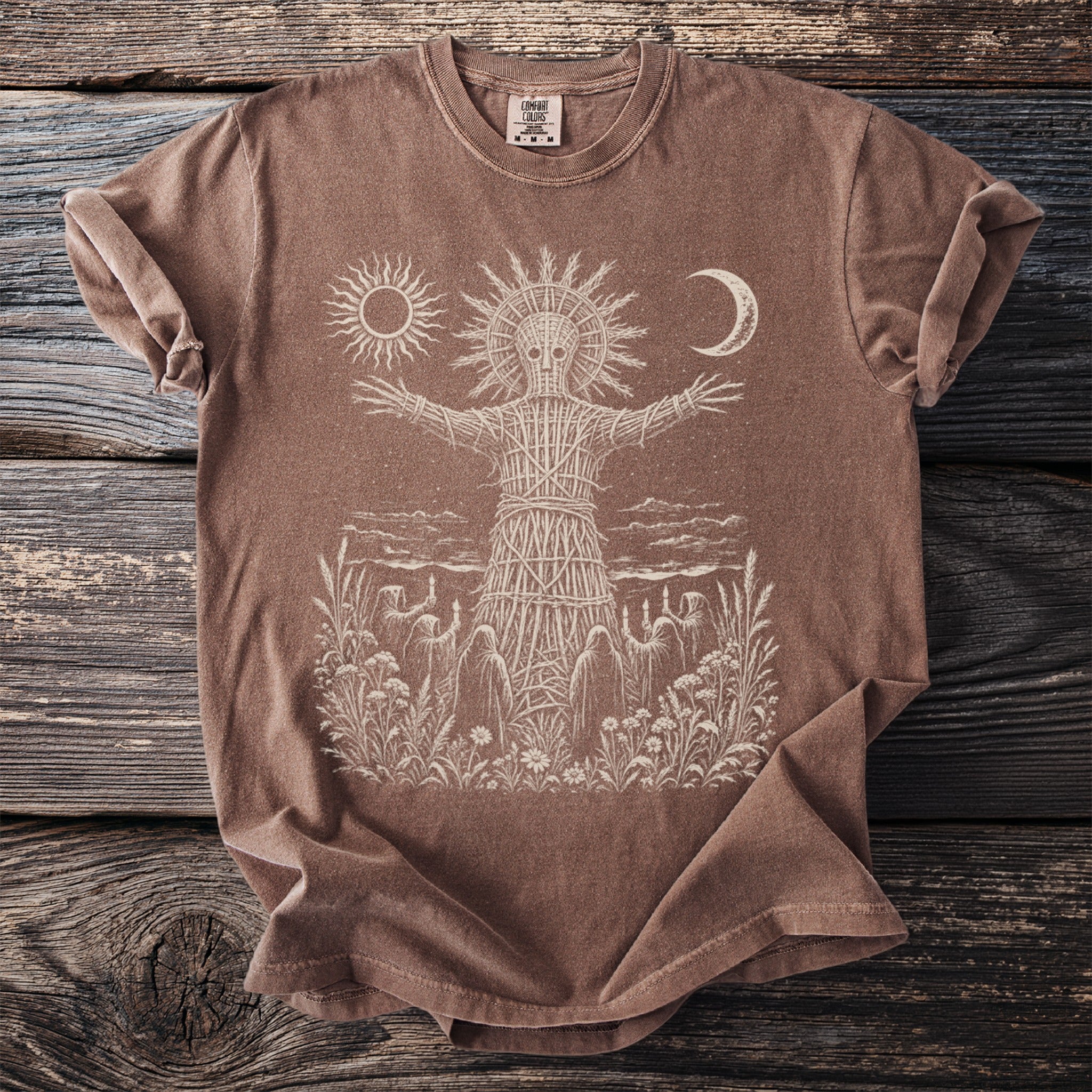 Brown t-shirt with a wicker figure, sun, moon, and figures holding candles.