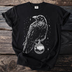 Black t-shirt with white raven perched on ornate ball and starry background.