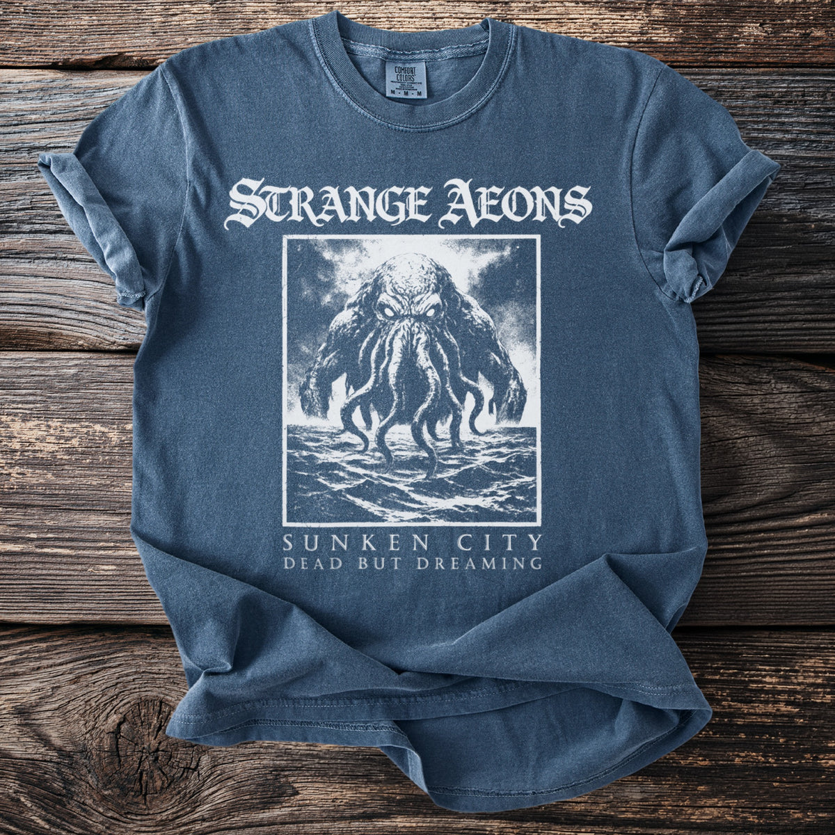 Blue t-shirt with "Strange Aeons" text and a sea monster graphic.