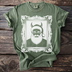 Green t-shirt with a white graphic of devil Santa Claus in a framed portrait.