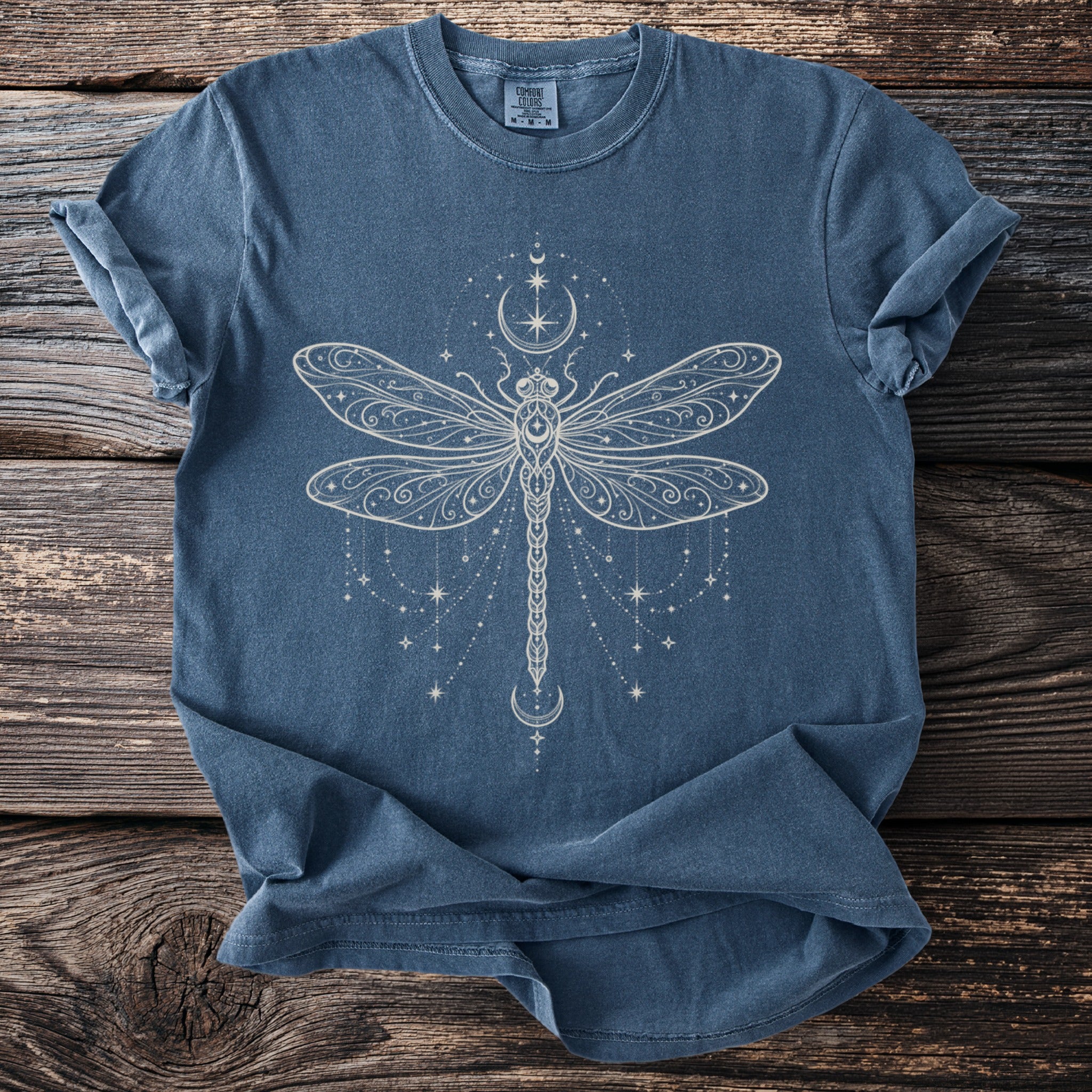 Blue t-shirt with a detailed white celestial dragonfly design and moon and star accents.