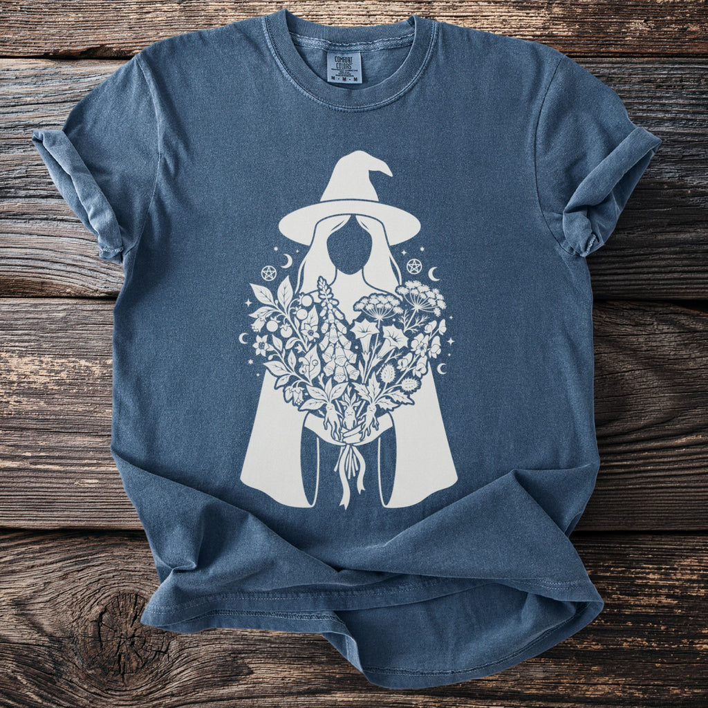 Blue t-shirt with a white witch and flower bouquet graphic and a Comfort Colors tag.