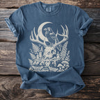 Blue t-shirt with a print of a crow on antlers over a skull, moon, and forest elements.
