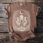 Brown Comfort Colors t-shirt with hooded figures around a campfire under a moon and trees.