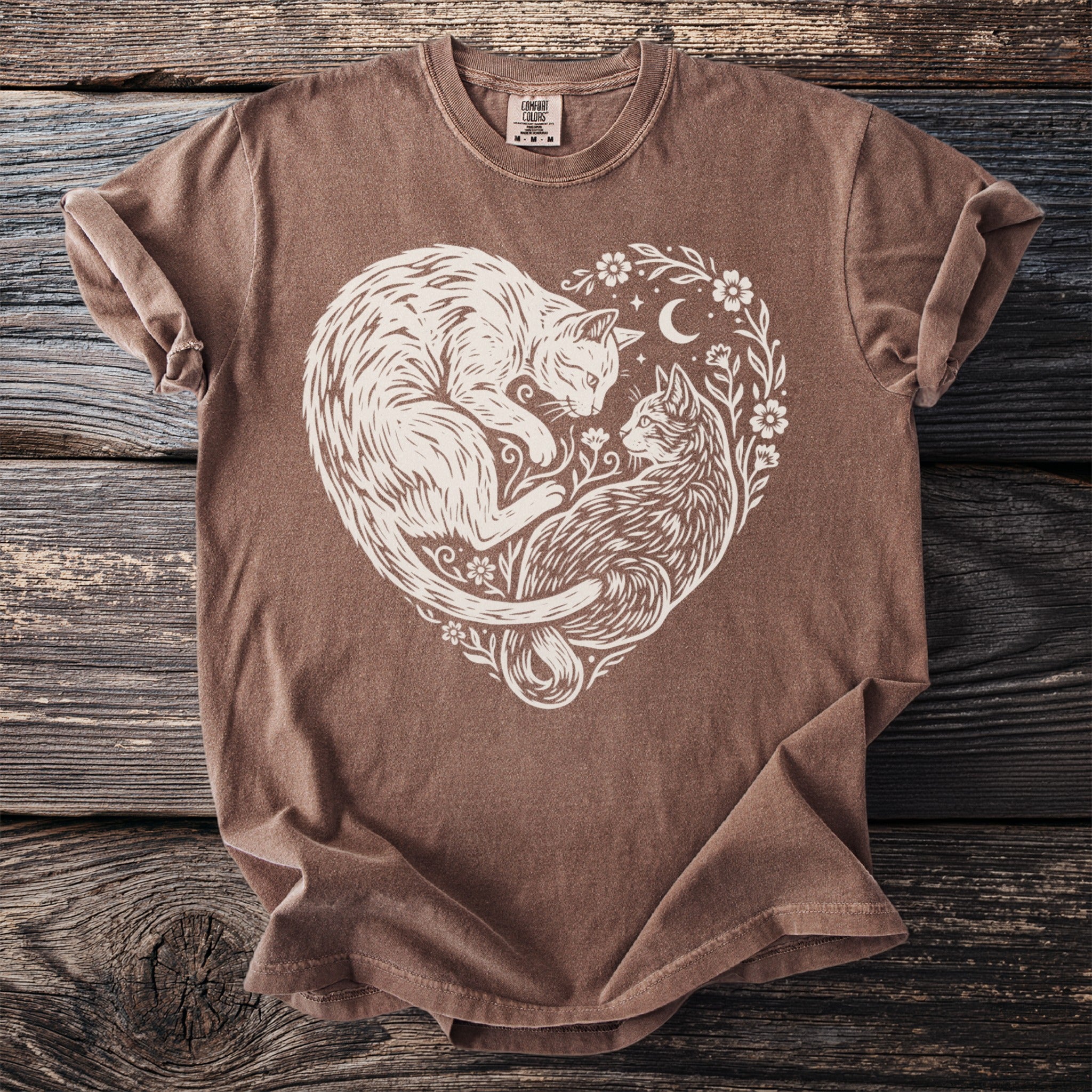 Brown t-shirt with stylized white cats forming a heart, surrounded by flowers and stars.