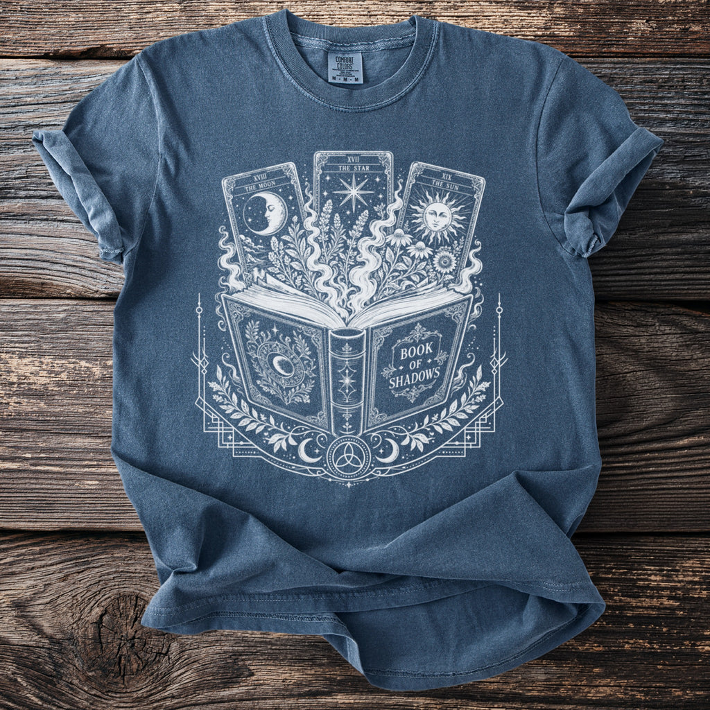 Blue t-shirt with a white graphic of an open book, tarot cards, and celestial elements.