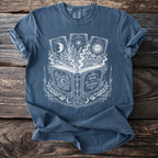 Blue t-shirt with a white graphic of an open book, tarot cards, and celestial elements.