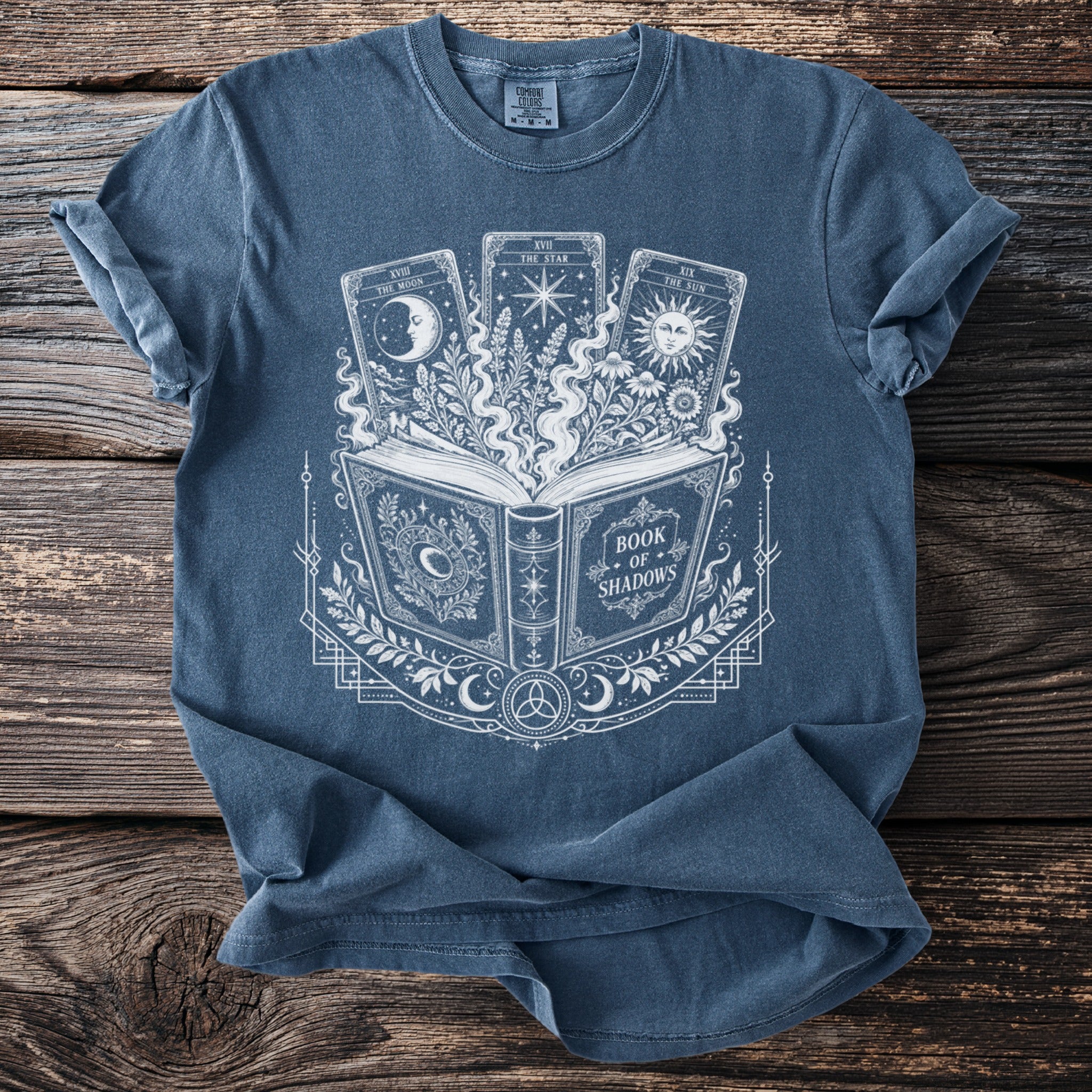 Blue t-shirt with a white graphic of an open book, tarot cards, and celestial elements.