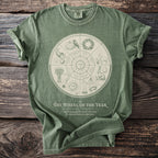 Green t-shirt features "The Wheel of the Year" Almanac illustrated with seasonal symbols.