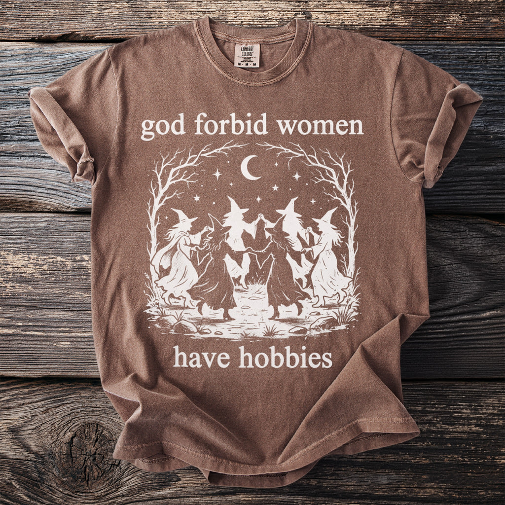 Brown t-shirt with witches dancing and text "god forbid women have hobbies".