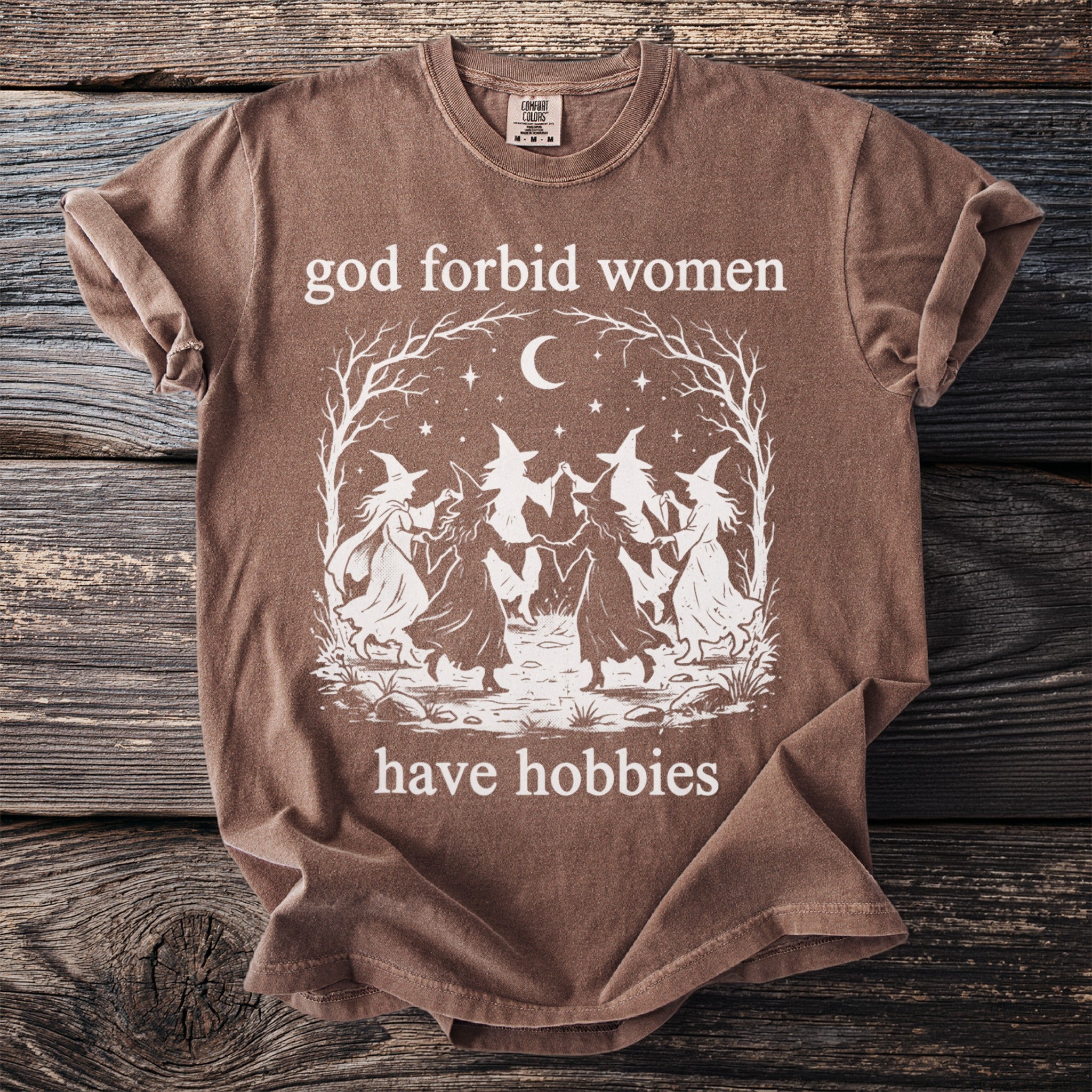 Brown t-shirt with witches dancing and text "god forbid women have hobbies".